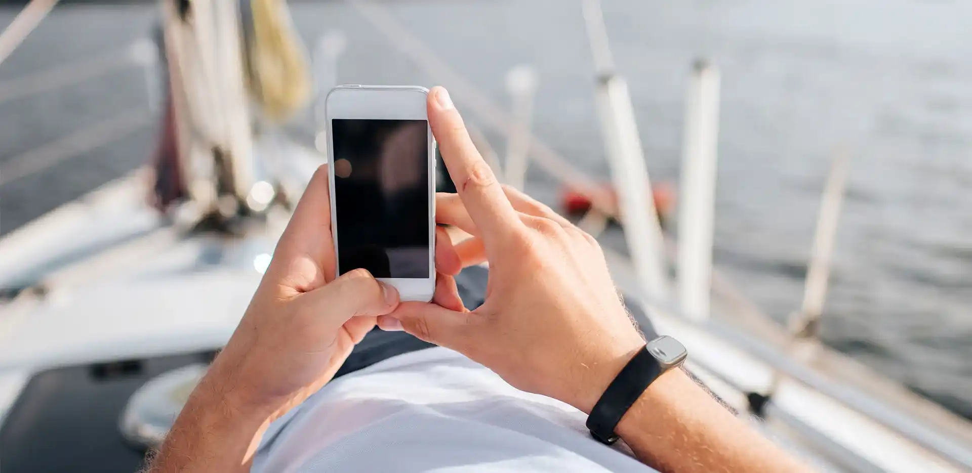 Ένας άντρας σε σκάφος χειρίζεται ένα κινητό με φόντο τη θάλασσα.